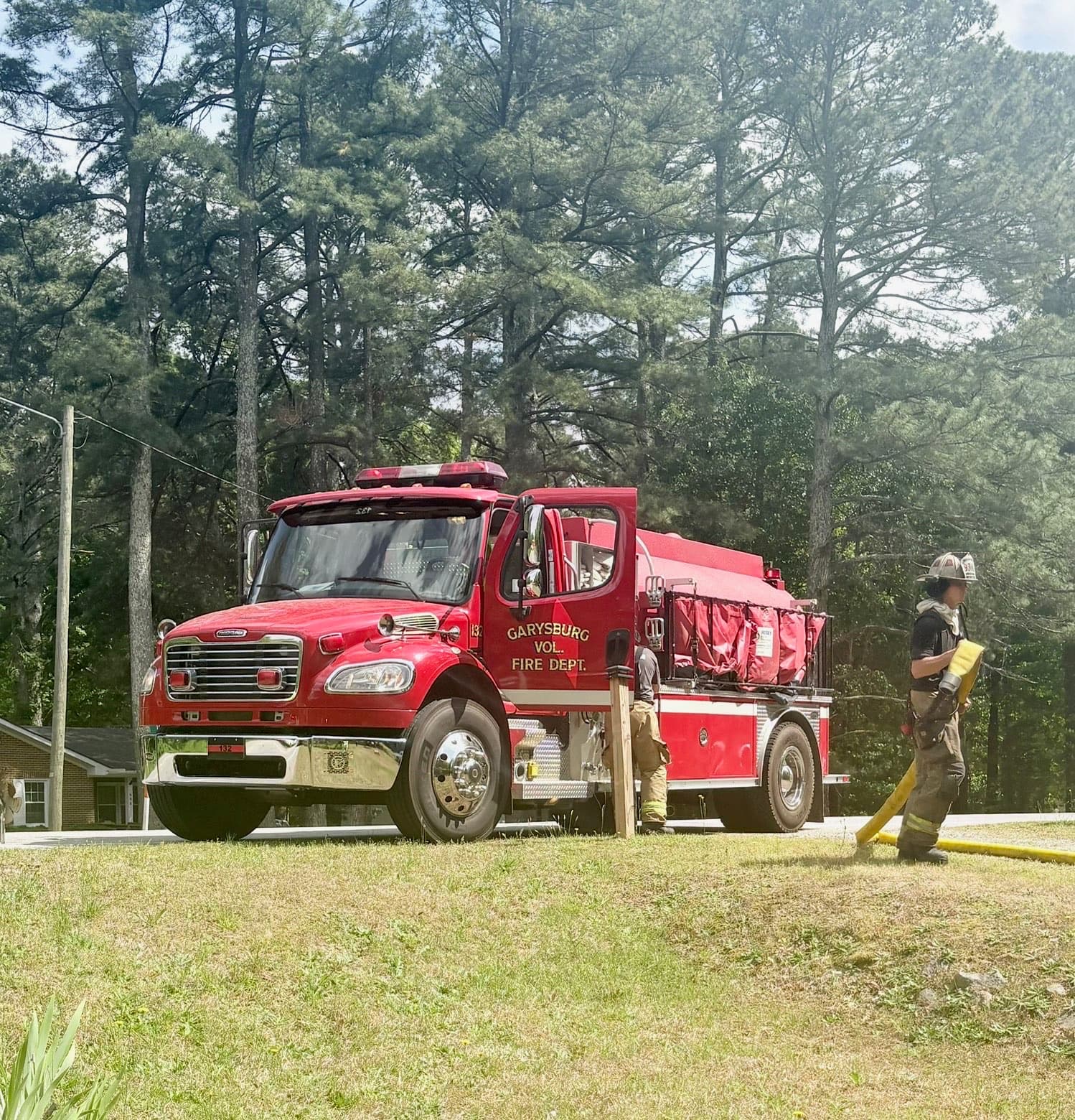 Garysburg Volunteer Fire Department tanker on a grassy roadside with a firefighter handling hose